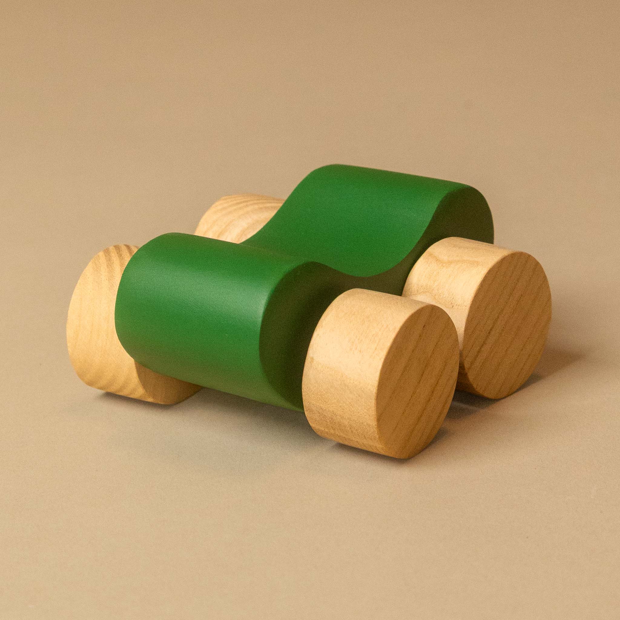 A modern wooden toy car with a wavy green body and natural light wood wheels, photographed on a solid beige background.