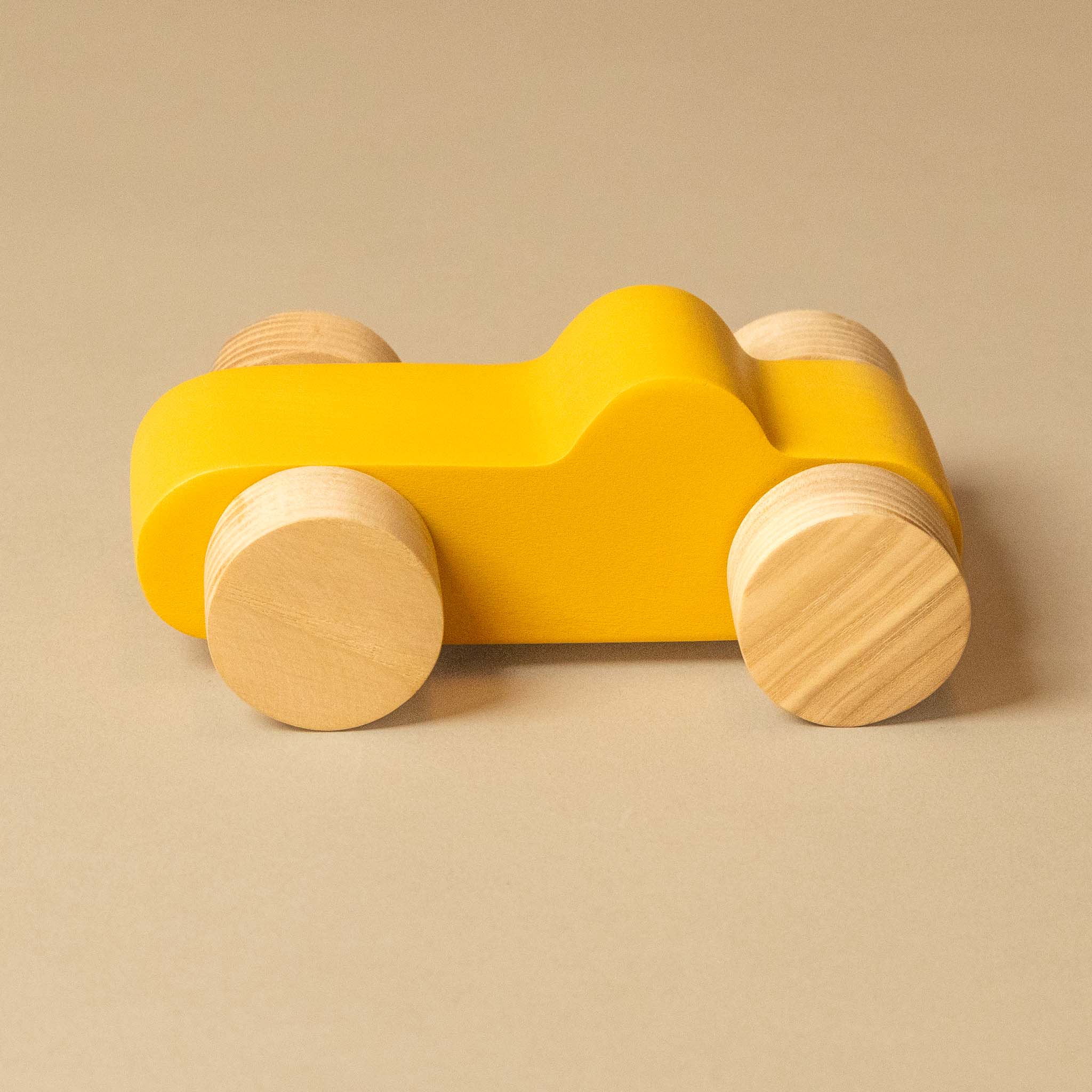 A minimalist wooden toy car with a bright yellow body and natural light wood wheels, photographed on a solid beige background.