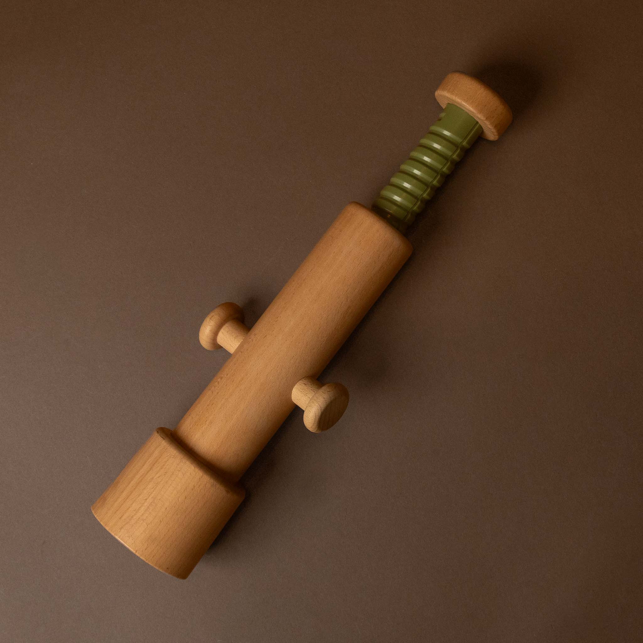 A wooden toy or tool with a light natural wood body, a green ribbed cylindrical section near the top, and small round knobs, photographed on a plain brown background.