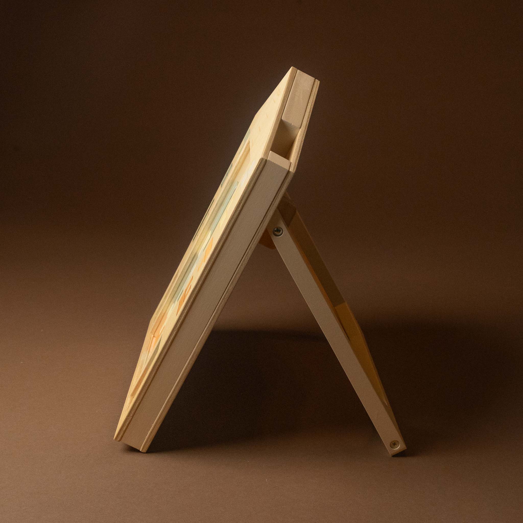 wooden-tetris-puzzle-playset A light natural wood folding display easel or stand, shown open and angled to display its inner panel, set against a solid dark brown studio background.