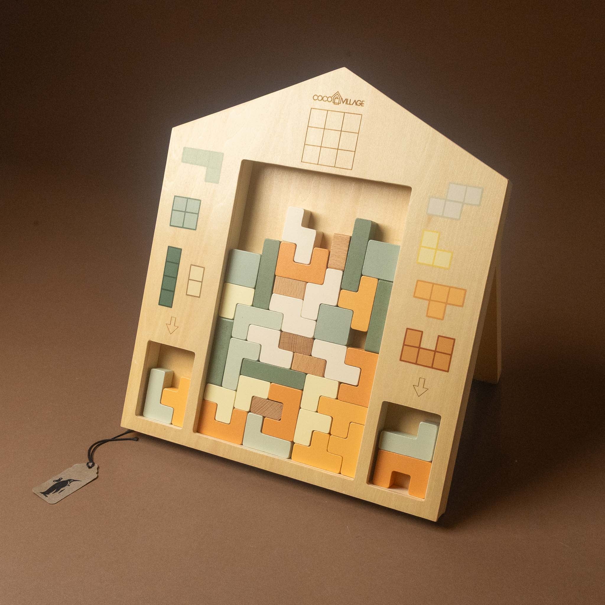 wooden-tetris-puzzle-playset house-shaped puzzle box with colorful interlocking geometric pieces inside, photographed on a warm brown studio background. 