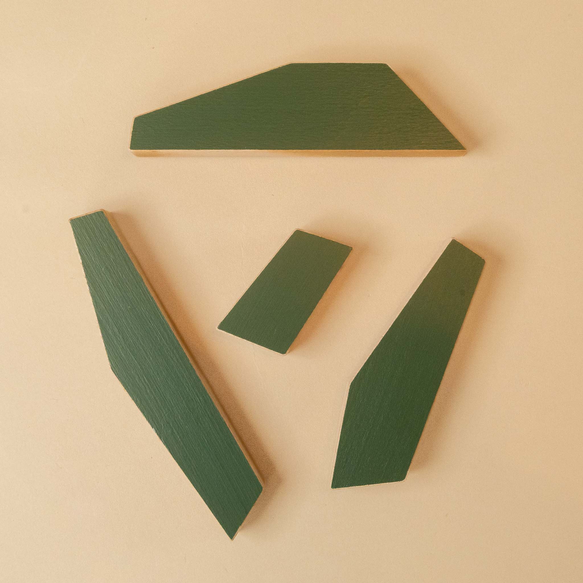 wooden-tree-pine Four dark green geometric wooden pieces arranged on a light beige background.