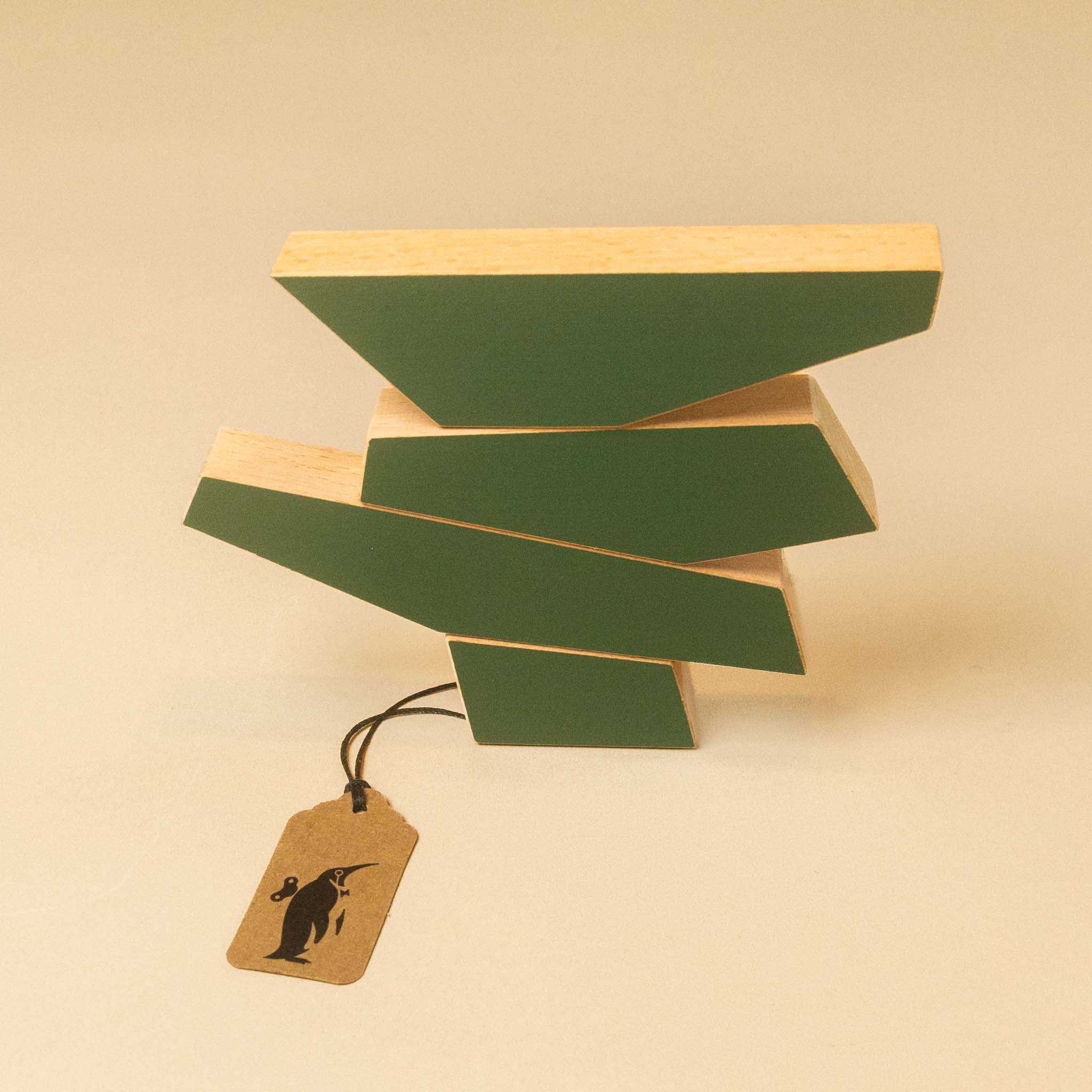 A modern geometric wooden block sculpture with alternating green and natural wood slats, shown with a small kraft paper tag on a warm beige background.