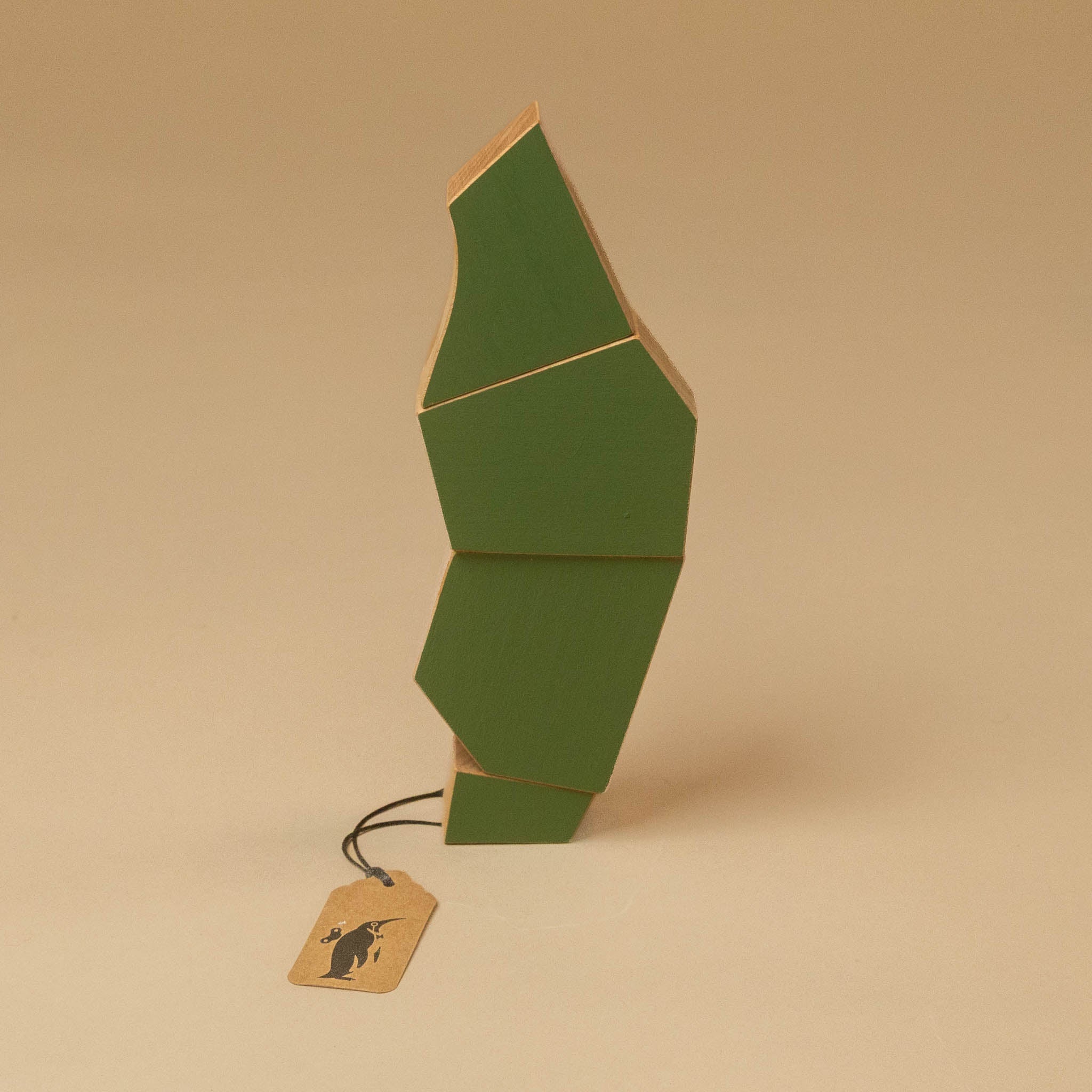 A green geometric, wooden-tree-poplar upright on a plain beige studio background, with a small hanging kraft paper tag attached by a black string.