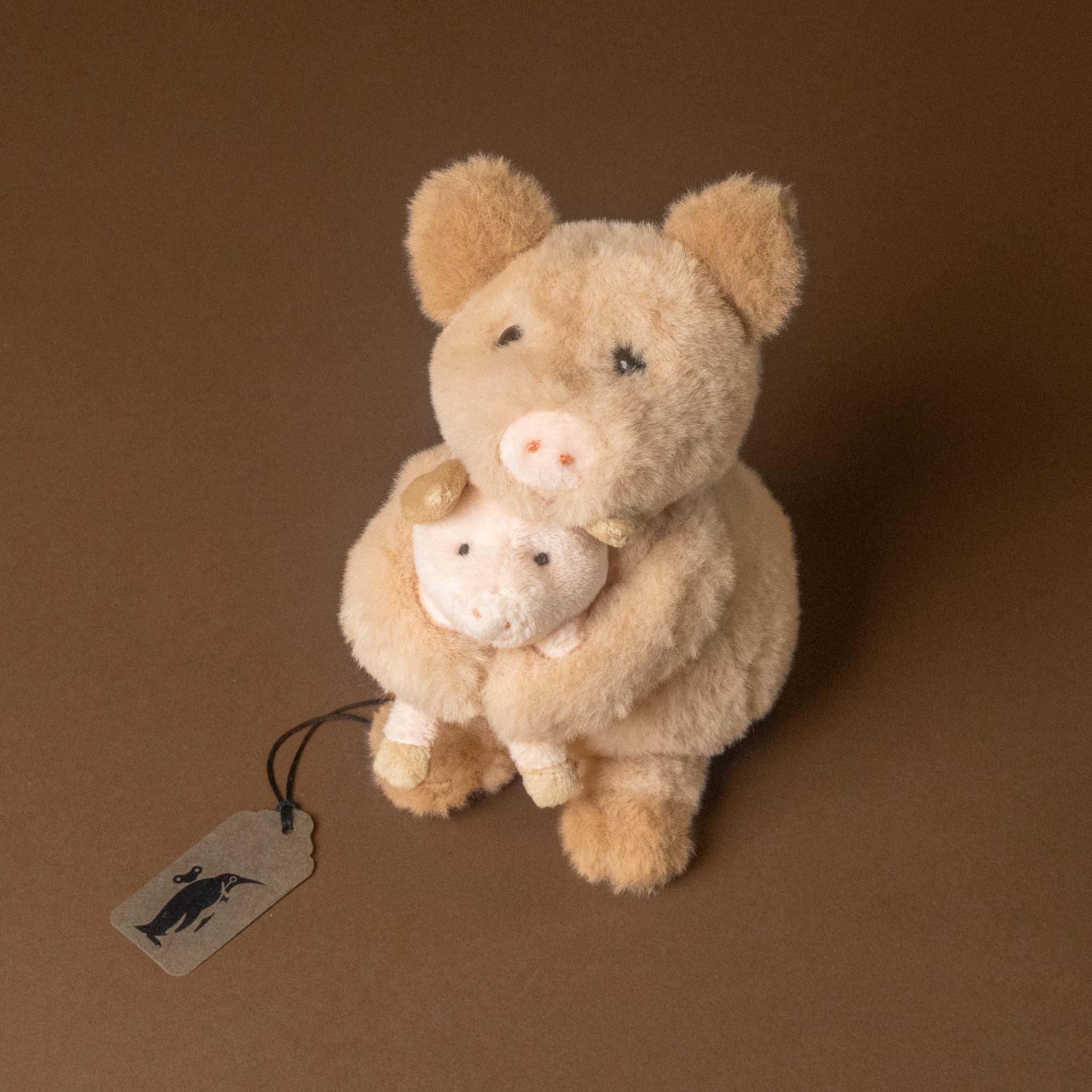 woodland-friends-pig-baby featuring a tan pig holding a smaller white pig, photographed against a solid brown studio background. 