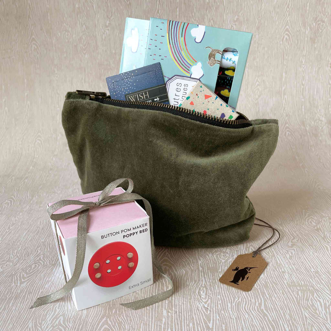 budding-artist-gift-set-showing-a-moss-green-velvet-pouch-holding-thoughtfulls-cards-magic-markers-block-crayons-and-sitting-next-to-a-red-button-pom-maker