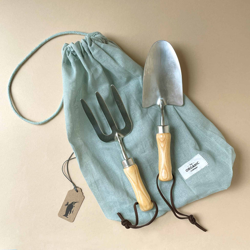 metal-gardening-tool-set-with-natural-wooden-handles-on-top-of-a-pale-blue-cotton-drawstring-bag