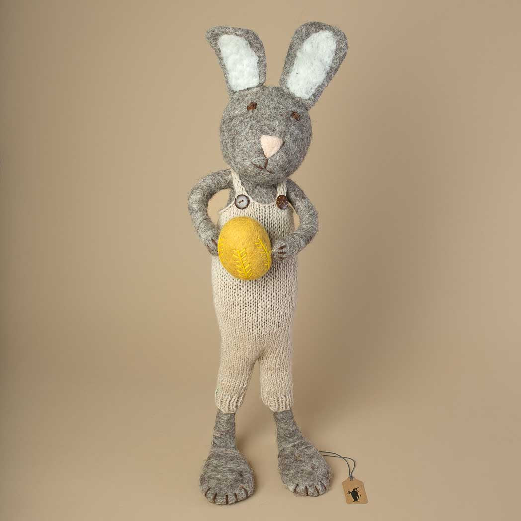 jumbo-sized-grey-felted-rabbit-with-knitted-beige-overall-holding-a-yellow-embroidered-egg-in-its-hands