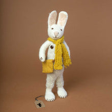 Load image into Gallery viewer, white-felted-rabbit-with-knitted-beige-overalls-and-brown-wooden-buttons-and-a-yellow-knitted-scarf-and-a-yellow-felted-bag-around-his-shoulders