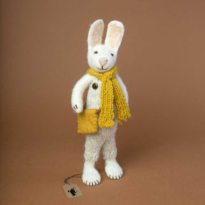 white-felted-rabbit-with-knitted-beige-overalls-and-brown-wooden-buttons-and-a-yellow-knitted-scarf-and-a-yellow-felted-bag-around-his-shoulders