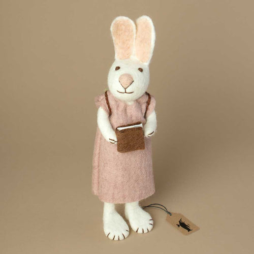white-felted-bunny-wearing-a-lavender-colored-dress-and-backpack-holding-a-brown-book-in-her-hands