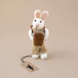 standing-white-felted-rabbit-with-sage-green-knitted-overall-holding-a-book-and-wearing-a-backpack