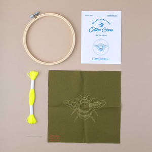 contents of the ebroidery  Bee kit showing yellow thread, a loop, the design of the bee on green cloth and the instructions booklet