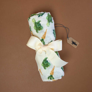 rolled-white-musselin-swaddle-with-orange-carrots-and-green-lettuce-pattern-sorounded-by-a-bright-yellow-ribbon