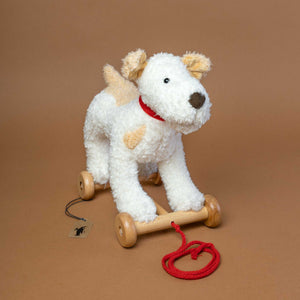 white-and-brown-stuffed-dog-on-wooden-wheels-with-red-pull-rope