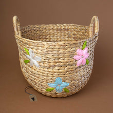Load image into Gallery viewer, light-brown-woven-round-basket-with-three-floweres-embroidered-in-colors-pink-blue-and-white